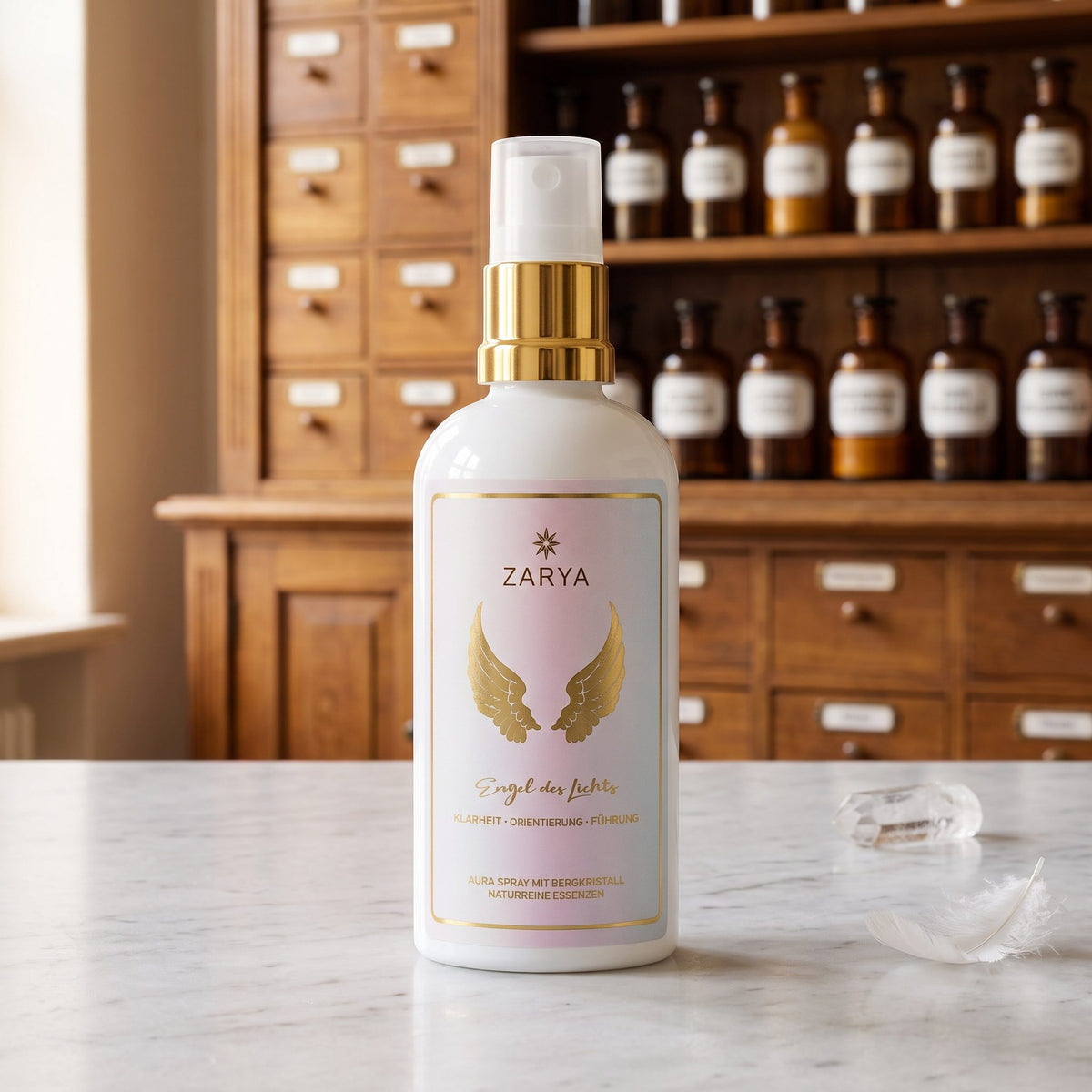 Engel des Lichts Aura Spray von Zarya: weiße Flasche mit goldenem Pumpring und goldenen Flügeln auf dem Etikett, auf der Marmortheke einer Apotheke, daneben ein klarer Bergkristall und eine weiße Feder