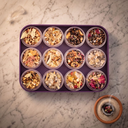 Ein Tontöpfchen mit glühender Räucherkohle und einer Prise Räucherwerk steht neben der violetten Schale mit den zwölf Döschen