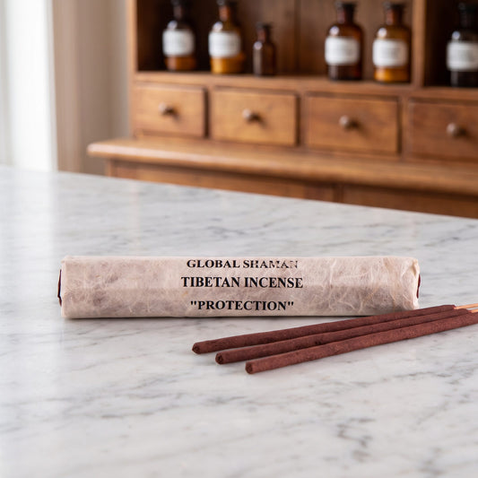 Tibetische Räucherstäbchen Schutz (Protection): Papierrolle mit Aufdruck Global Shaman Tibetan Incense auf einer Marmortheke, davor drei dunkelrote Stäbchen