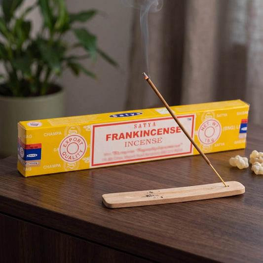Satya Frankincense Räucherstäbchen: glimmendes Räucherstäbchen mit feinem Rauch im Holzhalter, dahinter die Packung, auf einem Sideboard am Abend