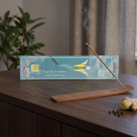 Engel des Erwachens Räucherstäbchen Holy Smokes: glimmendes Räucherstäbchen mit feinem Rauch im Holzhalter, dahinter die Packung, auf einem Sideboard am Abend