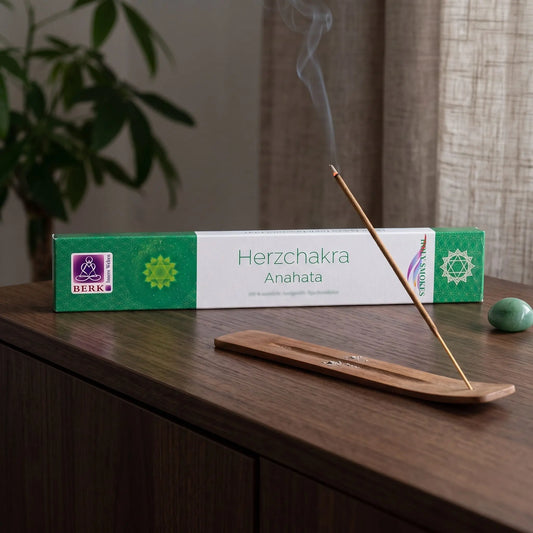 Herzchakra Räucherstäbchen Holy Smokes: glimmendes Räucherstäbchen mit feinem Rauch im Holzhalter, dahinter die Packung, auf einem Sideboard am Abend