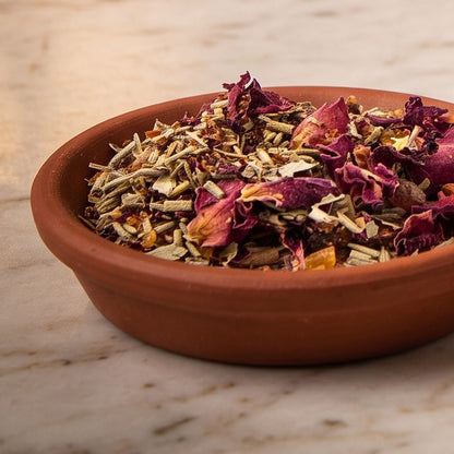 Loslassen I, Räuchermischung der Reihe Einfach Räuchern von Berk, 50 ml im Korkglas: Nahaufnahme der Terracottaschale mit Rosenblüten und Rosmarin vor der warmen, unscharfen Abendapotheke – Spirit of Gaia