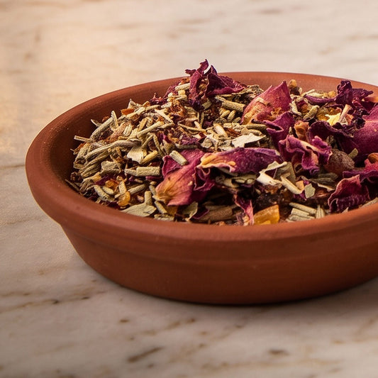 Loslassen I, Räuchermischung der Reihe Einfach Räuchern von Berk, 50 ml im Korkglas: Nahaufnahme der Terracottaschale mit Rosenblüten und Rosmarin vor der warmen, unscharfen Abendapotheke – Spirit of Gaia
