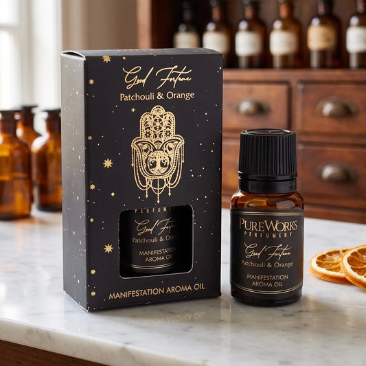 Aromaöl Good Fortune (Patchouli & Orange) von Pure Works: Fläschchen und schwarze Schachtel mit Goldprägung auf Marmortheke vor Apothekerschrank, daneben getrocknete Orangenscheiben – Spirit of Gaia