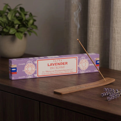 Satya Lavender Räucherstäbchen: glimmendes Räucherstäbchen mit feinem Rauch im Holzhalter, dahinter die Packung, auf einem Sideboard am Abend