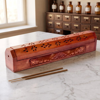 Kistchen/Halter für Räucherstäbchen Lotus: geschlossenes Holzkistchen mit Lotus-Schnitzerei auf einer Marmortheke vor einem Apothekerschrank, daneben zwei lose Räucherstäbchen – Spirit of Gaia