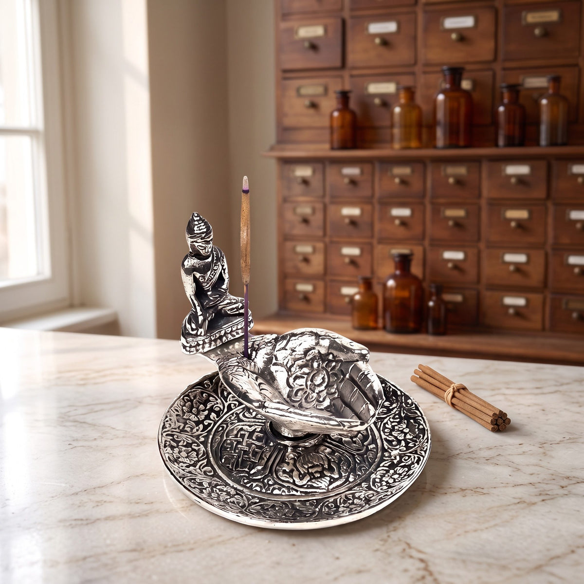 Räucherstäbchenhalter Hände mit Buddha auf einer Marmortheke vor einem Apothekerschrank – Spirit of Gaia