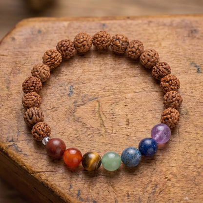 Draufsicht auf das Chakra Rudraksha Armband auf altem Holz: sieben Steine von Rotbraun bis Violett zwischen zerfurchten Rudraksha-Samen