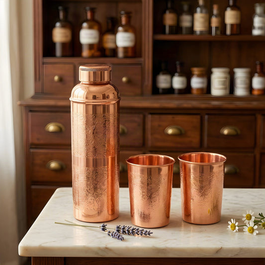 Kupfer-Trinkset mit Blumengravur, Flasche und zwei Becher, auf Marmortheke vor Apothekerschrank – Spirit of Gaia