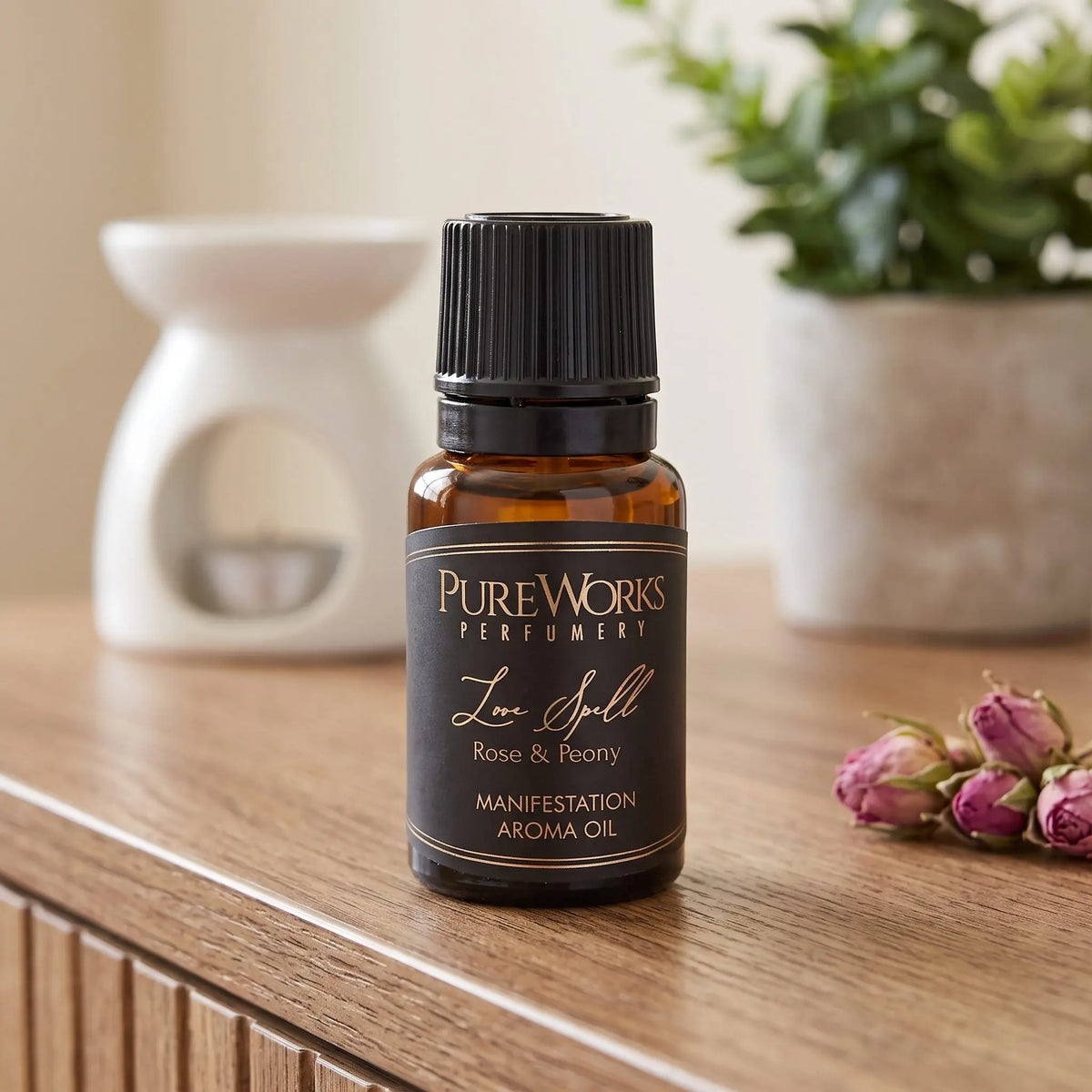 Aromaöl Love Spell (Rose & Pfingstrose): Fläschchen auf einem Holz-Sideboard im Wohnzimmer, im Hintergrund eine weiße Duftlampe, daneben getrocknete Rosenknospen