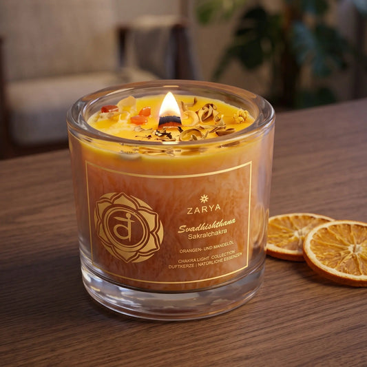 Chakra-Kerze Sakralchakra Svadhishthana mit Orangencalcit und Citrin, Duft Orange und Mandel: brennende Kerze mit kleiner Flamme am Abend auf einer dunklen Holzplatte im Wohnzimmer, daneben getrocknete Orangenscheiben – Spirit of Gaia