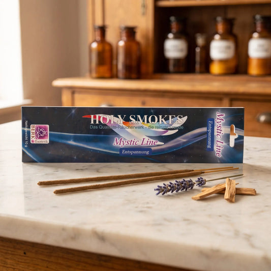 Entspannung Räucherstäbchen Holy Smokes Mystic Line: Packung auf einer Marmortheke vor einem Apothekerschrank, davor zwei lose Räucherstäbchen, getrockneter Lavendel und Sandelholz – Spirit of Gaia