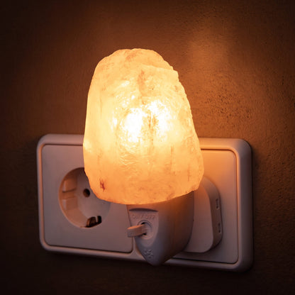 Salzkristall-Nachtlicht Natur in einer Steckdose leuchtet warm orange vor einer dunklen Putzwand