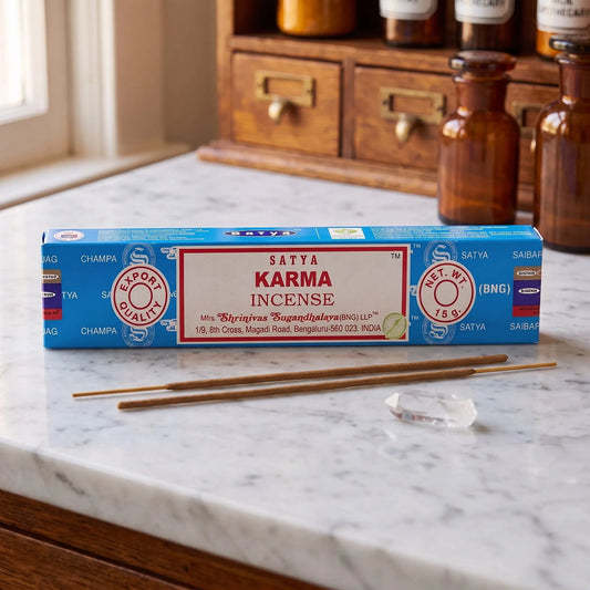 Satya Karma Räucherstäbchen: 15-g-Packung auf einer Marmortheke vor einem Apothekerschrank, daneben zwei lose Räucherstäbchen – Spirit of Gaia