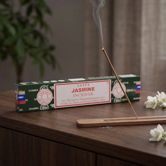 Satya Jasmine Räucherstäbchen: glimmendes Räucherstäbchen mit feinem Rauch im Holzhalter, dahinter die Packung, auf einem Sideboard am Abend