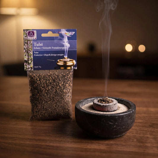 Tulsi (Heiliges Basilikum), sortenreines Räucherwerk von Berk, 10 g: eine Prise Tulsi glimmt auf der Räucherkohle, dahinter die Tüte, feiner Rauch steigt auf einer dunklen Holzplatte am Abend auf – Spirit of Gaia