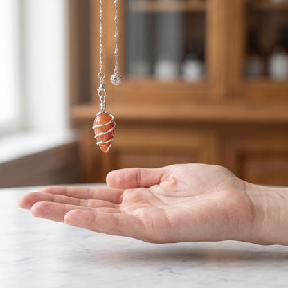 Das Karneol-Spiralpendel hängt ruhig an seiner silberfarbenen Kette über einer offenen Handfläche