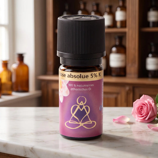 Ätherisches Öl Rose absolue: Fläschchen aus Braunglas auf Marmortheke vor Apothekerschrank, daneben eine Rosenblüte – Spirit of Gaia
