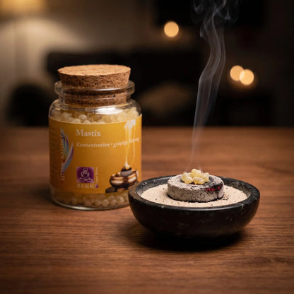 Mastix griechisch, reines Räucherharz von Berk, 60 ml im Korkglas: glimmende Räucherkohle mit einigen Mastixtränen in einer Specksteinschale, dahinter das Korkglas, feiner Rauch steigt auf einer dunklen Holzplatte am Abend auf – Spirit of Gaia