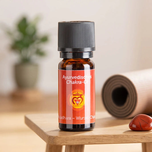 Ayurvedisches Chakra-Öl Muladhara (Wurzel-Chakra): 10-ml-Fläschchen auf einem Holzhocker neben einer gerollten Yogamatte, daneben roter Jaspis