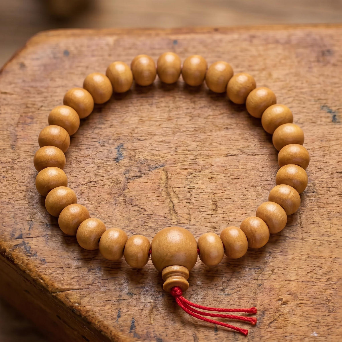 Draufsicht auf das Power-Bracelet Sandelholz auf altem Holz: Reihe aus Sandelholzperlen mit größerer Guruperle und rotem Faden