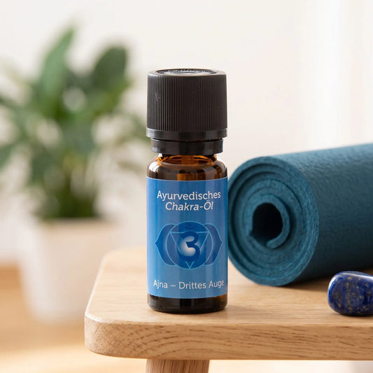 Ayurvedisches Chakra-Öl Ajna (Stirn-Chakra): 10-ml-Fläschchen auf einem Holzhocker neben einer gerollten Yogamatte, daneben Lapislazuli