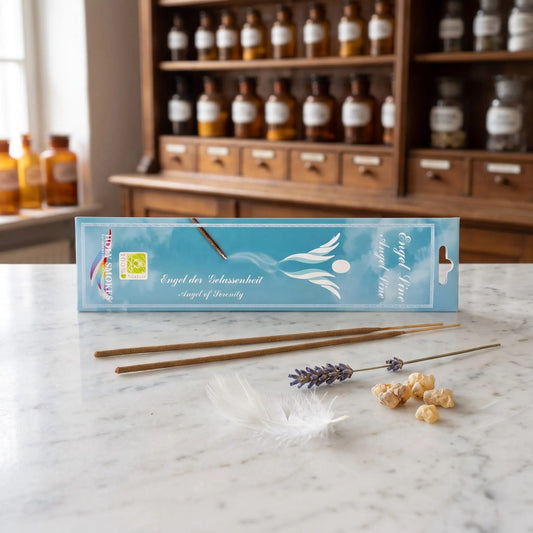 Engel der Gelassenheit Räucherstäbchen Holy Smokes: Packung auf einer Marmortheke vor einem Apothekerschrank, davor zwei lose Räucherstäbchen, eine weiße Feder, getrockneter Lavendel und Guggulharz – Spirit of Gaia