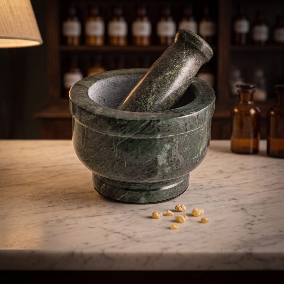 Mörser aus grünem Marmor mit Stößel auf der Marmortheke einer Apotheke am Abend, davor einige Harzkörner