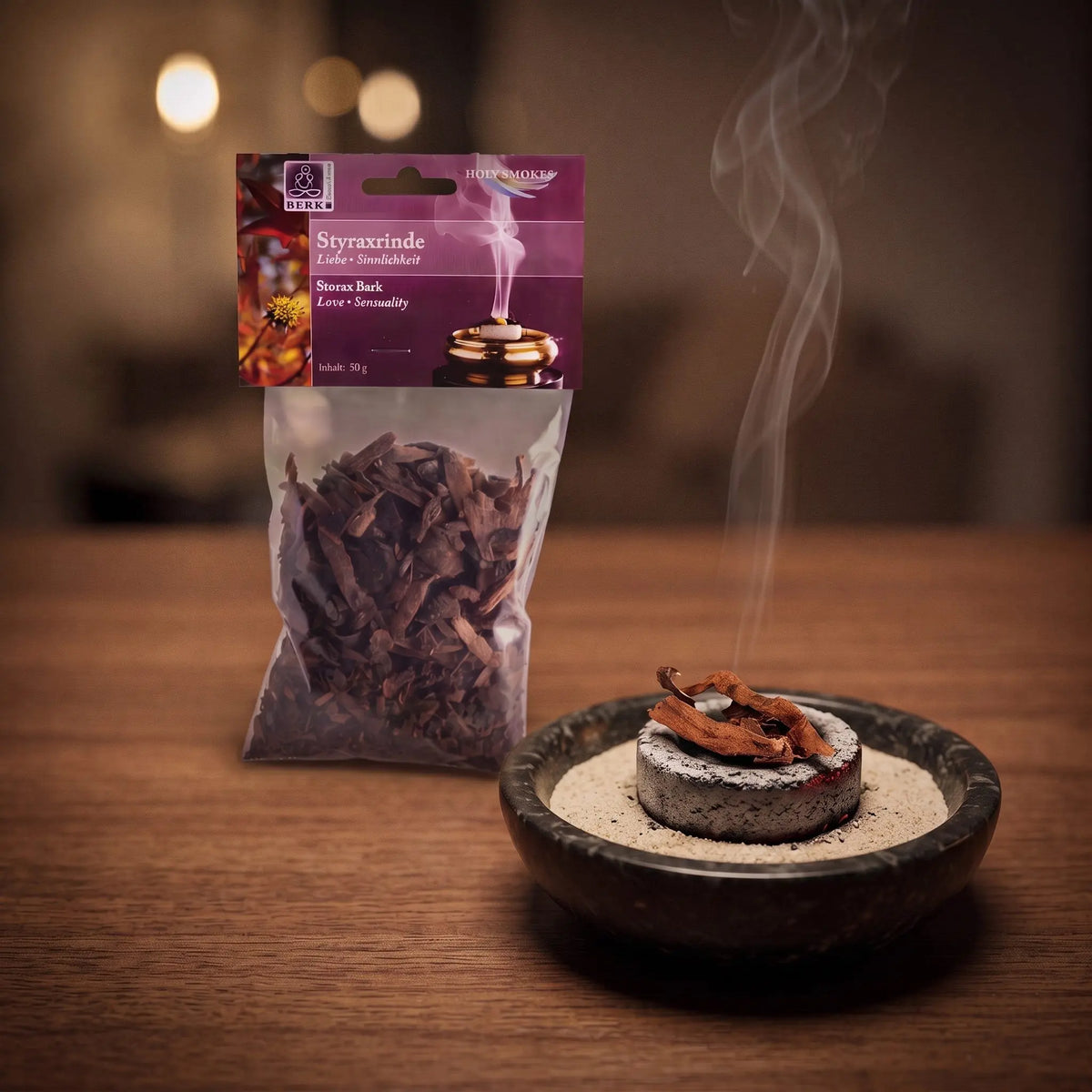 Styraxrinde, sortenreines Räucherwerk von Berk, 50 g: einige Stücke Styraxrinde glimmen auf der Räucherkohle, dahinter die Tüte, feiner Rauch steigt auf einer dunklen Holzplatte am Abend auf – Spirit of Gaia