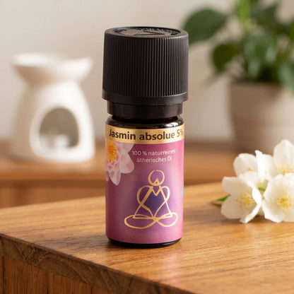 Ätherisches Öl Jasmin absolue: Fläschchen auf einem Holz-Sideboard im Wohnzimmer, im Hintergrund eine weiße Duftlampe, daneben Jasminblüten