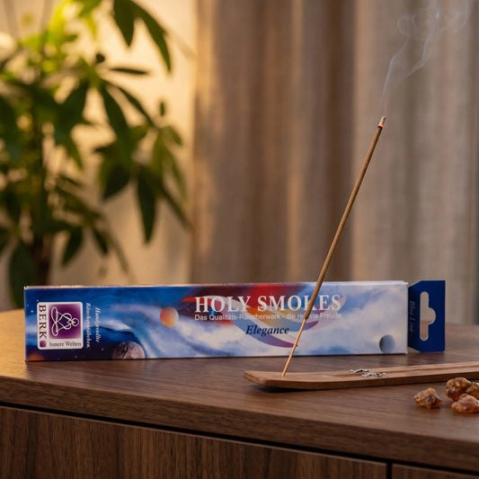 Elegance Räucherstäbchen Blue Line: glimmendes Räucherstäbchen mit feinem Rauch im Holzhalter, dahinter die Packung, auf einem Sideboard am Abend