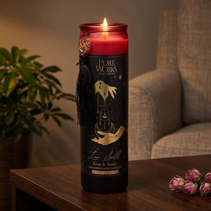 Manifestationskerze Love Spell (Rose & Pfingstrose): brennende Glaskerze auf einem dunklen Holztisch im Wohnzimmer am Abend, daneben getrocknete Rosenknospen