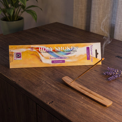 Lavendel Räucherstäbchen Natural Line: glimmendes Stäbchen im Holzhalter auf einem dunklen Sideboard, dahinter die Packung, am Abend