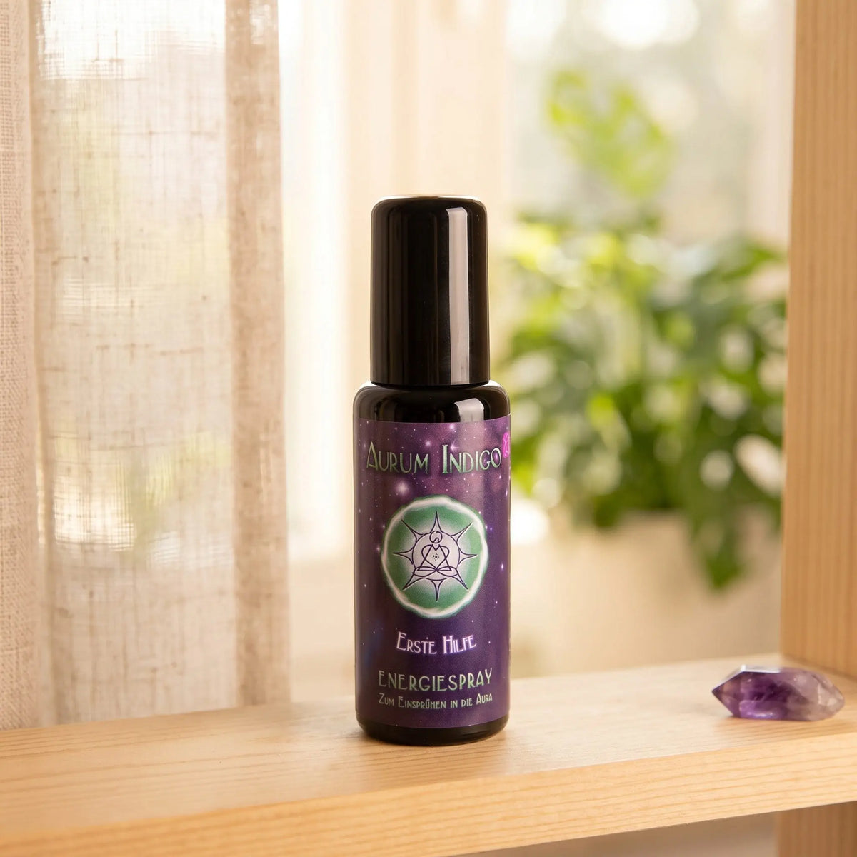 Energiespray Aurum Indigo Erste Hilfe: Sprühflasche auf einem hellen Holzregal am Fenster mit Leinenvorhang, daneben ein Amethyst