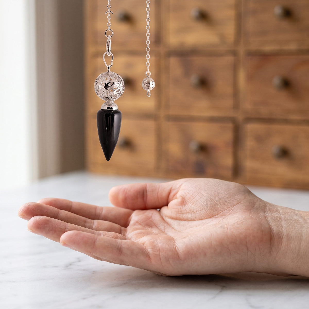 Das Obsidian-Pendel hängt ruhig an seiner silberfarbenen Kette über einer offenen Handfläche