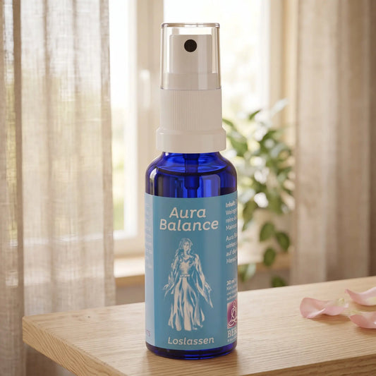 Energiespray Loslassen (Aura Balance): Sprühflasche auf einem hellen Holzregal am Fenster mit Leinenvorhang, daneben Rosenblütenblätter