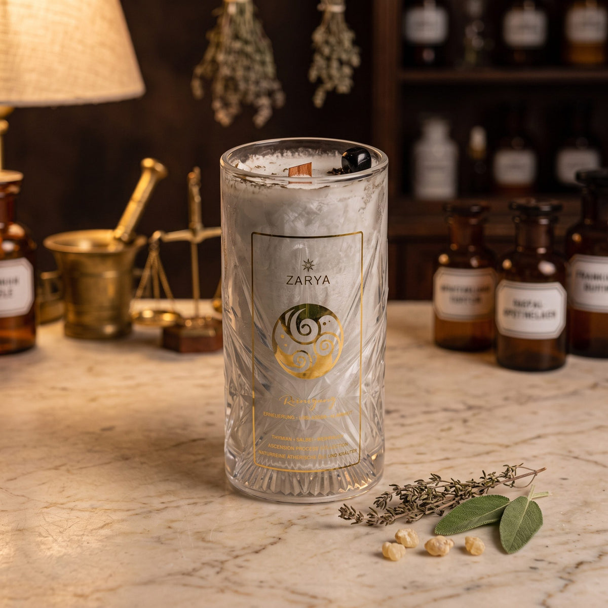 Zarya Kerze Reinigung im hohen Glas mit Schliffmuster und goldenem Etikett auf der Marmortheke einer Apotheke am Abend, daneben Thymian, Salbei und Weihrauchkörner