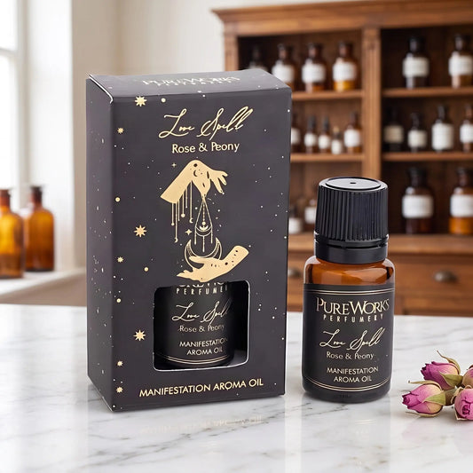 Aromaöl Love Spell (Rose & Pfingstrose) von Pure Works: Fläschchen und schwarze Schachtel mit Goldprägung auf Marmortheke vor Apothekerschrank, daneben getrocknete Rosenknospen – Spirit of Gaia