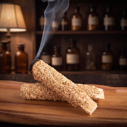 Ein Palo-Santo-Stab mit Eukalyptus glimmt an der geschwärzten Spitze, feiner Rauch steigt auf, der zweite Stab liegt daneben auf einer Holzschale