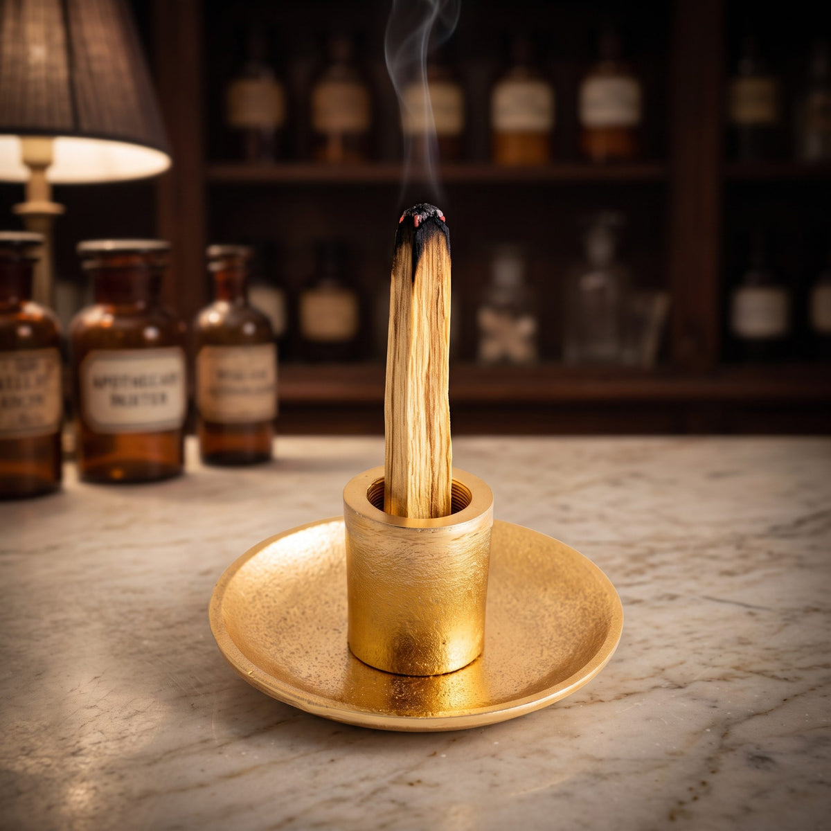Ein Palo-Santo-Stab glimmt aufrecht in der goldenen Hülse, feiner Rauch steigt auf