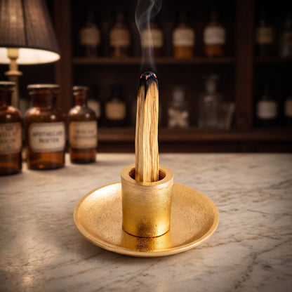 Ein Palo-Santo-Stab glimmt aufrecht in der goldenen Hülse, feiner Rauch steigt auf