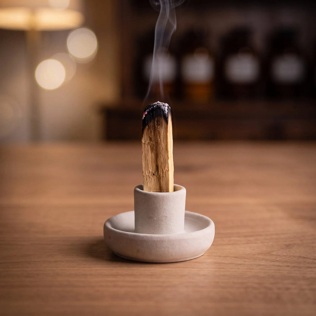 Ein Palo-Santo-Stab glimmt aufrecht im Tonhalter, feiner Rauch steigt auf