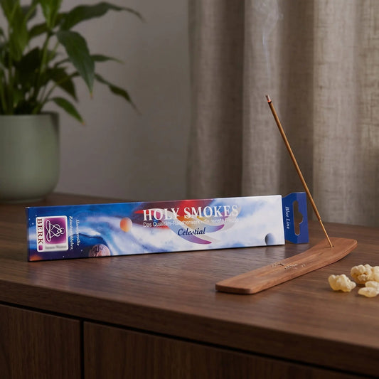 Celestial Räucherstäbchen Blue Line: glimmendes Räucherstäbchen mit feinem Rauch im Holzhalter, dahinter die Packung, auf einem Sideboard am Abend