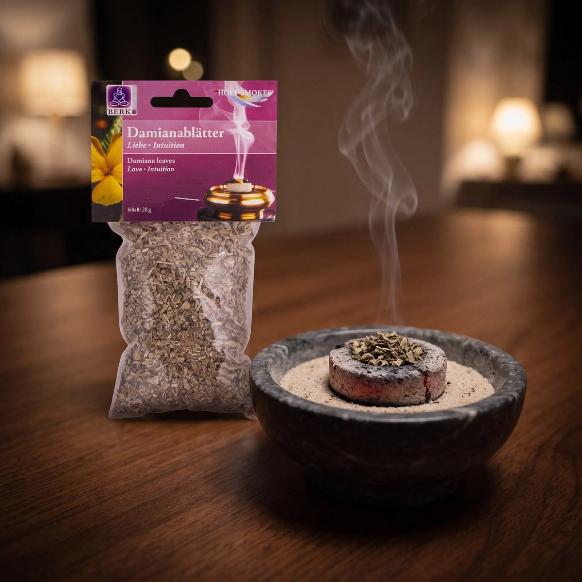 Damianablätter, sortenreines Räucherwerk von Berk, 20 g: eine Prise Damianablätter glimmt auf der Räucherkohle, dahinter die Tüte, feiner Rauch steigt auf einer dunklen Holzplatte am Abend auf – Spirit of Gaia