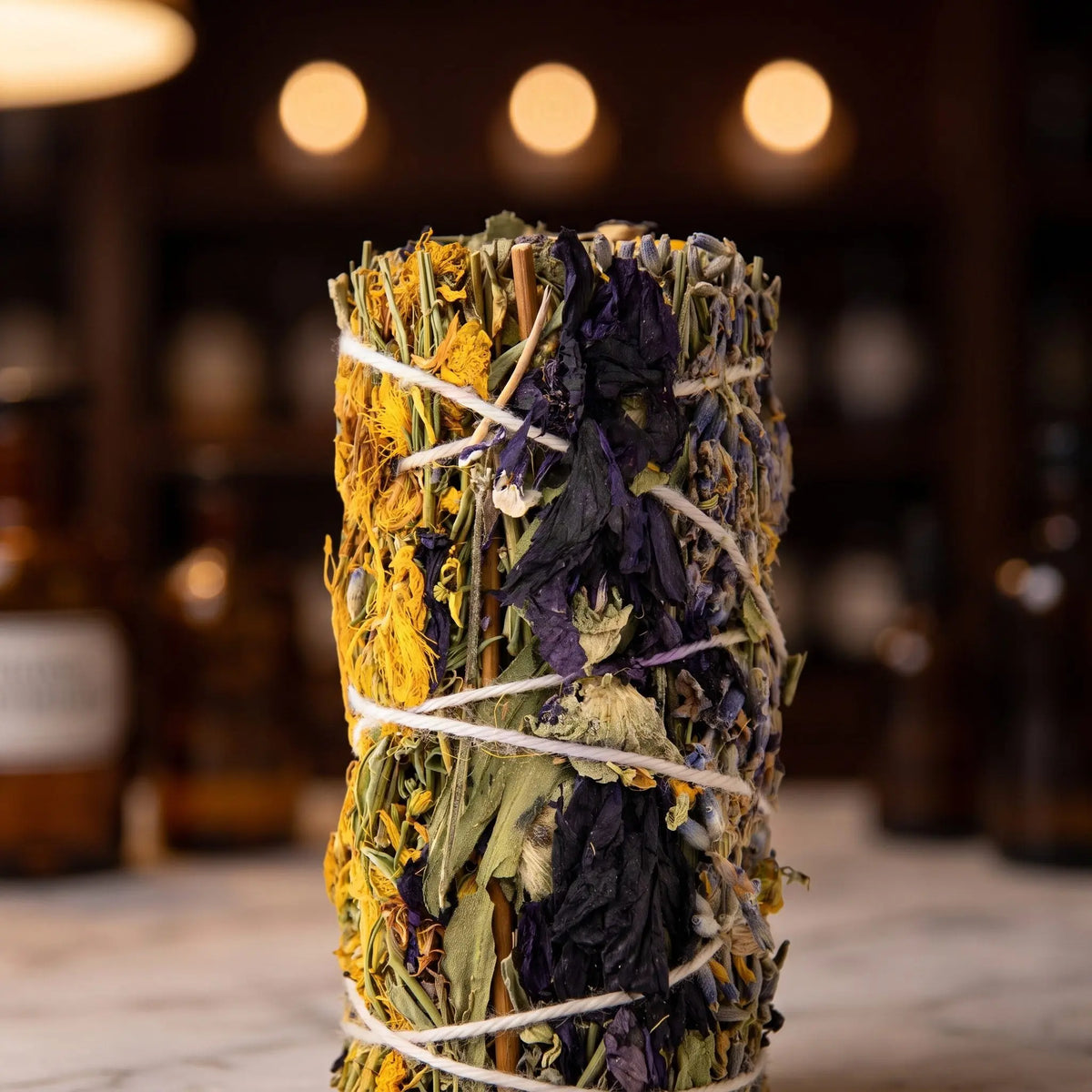 Nahaufnahme des Räucherbündels Innere Ruhe: gelbe Johanniskrautblüten, violette Malvenblüten, Lavendel und helles Garn