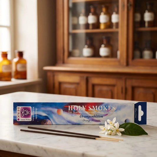 Orangenblüten Räucherstäbchen Holy Smokes Blue Line: Packung auf einer Marmortheke vor einem Apothekerschrank, davor zwei lose Räucherstäbchen und weiße Orangenblüten – Spirit of Gaia