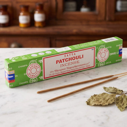 Satya Patchouli Räucherstäbchen: 15-g-Packung auf einer Marmortheke vor einem Apothekerschrank, daneben zwei lose Räucherstäbchen – Spirit of Gaia