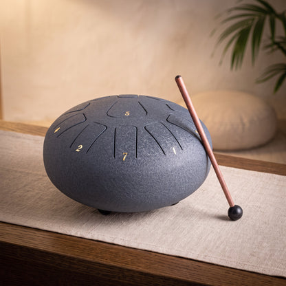 Große dunkelblaue Steeldrum mit Klangstab auf einem Leinenläufer, dahinter ein warmer Meditationsraum