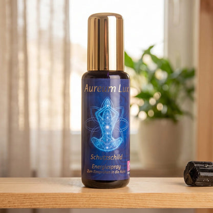 Energiespray Aureum Lux Schutzschild: Sprühflasche auf einem hellen Holzregal am Fenster mit Leinenvorhang, daneben ein schwarzer Turmalin